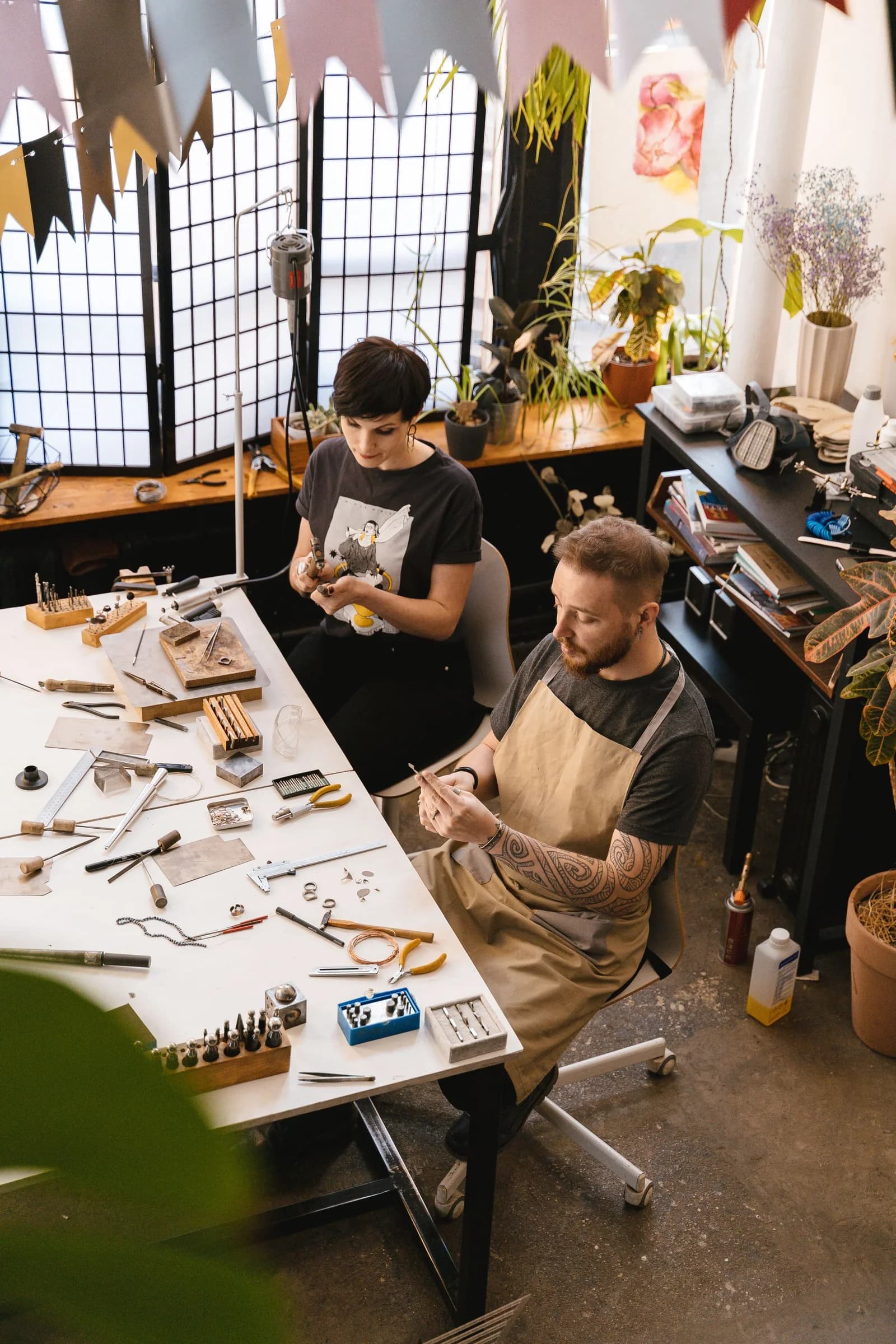Twee mensen werken geconcentreerd met handgereedschap aan sieraden in een werkplaats.