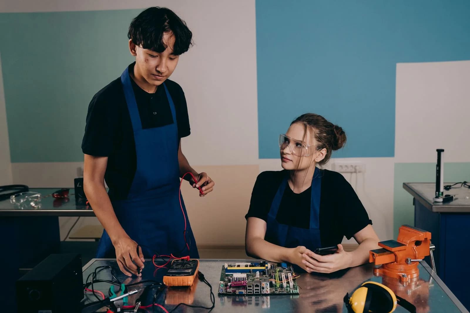 Twee technici onderzoeken elektronica met een multimeter.